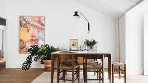 A dining area with a wooden table and chairs, a potted plant, and a painting on the wall.
