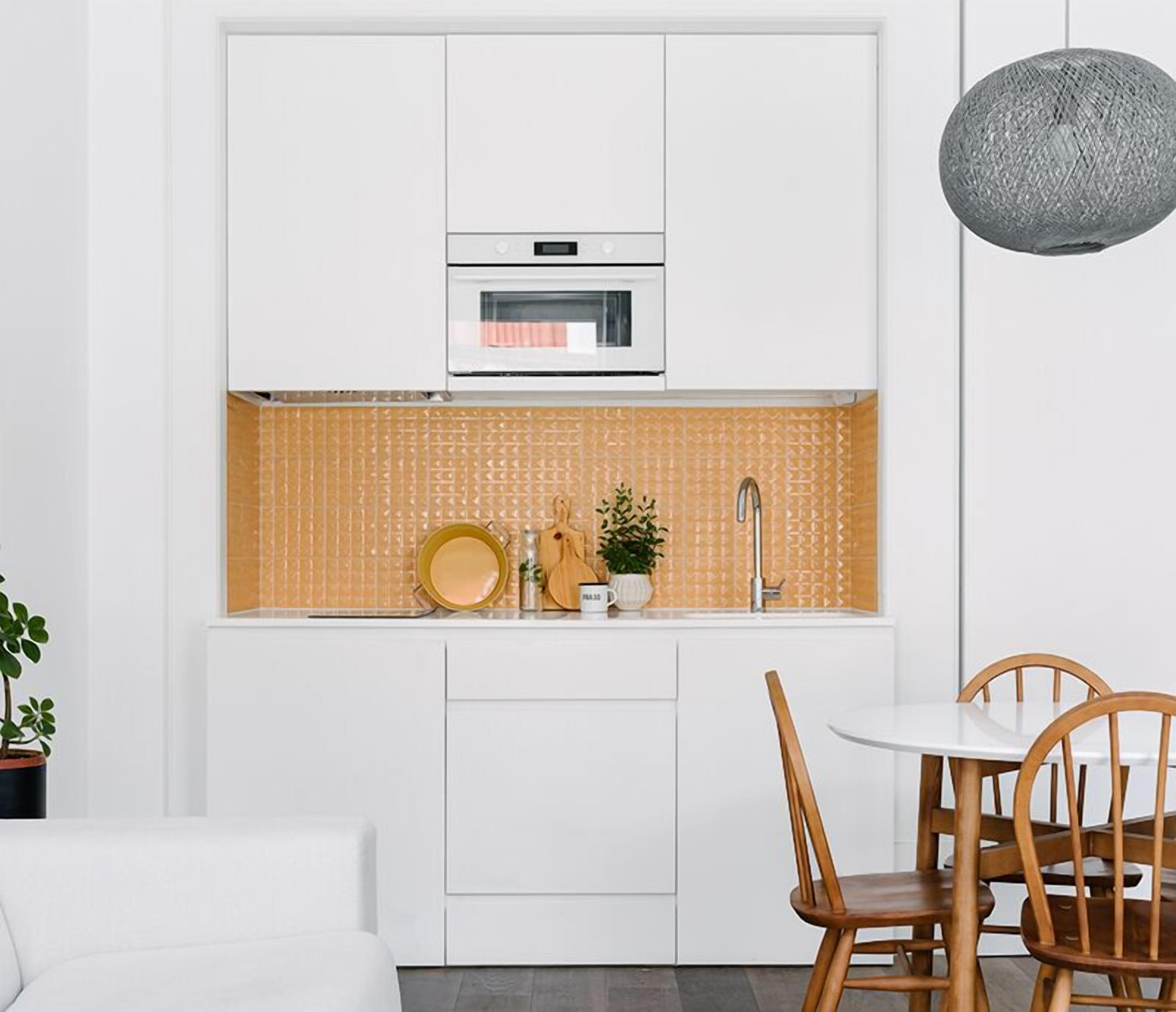 A compact kitchen with white cabinetry, a microwave, a sink with a modern faucet, and a dining area with a round table and wooden chairs.