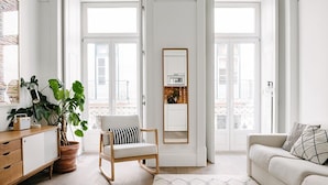 A bright living room with a sofa, a chair, a wooden cabinet, and a large potted plant.