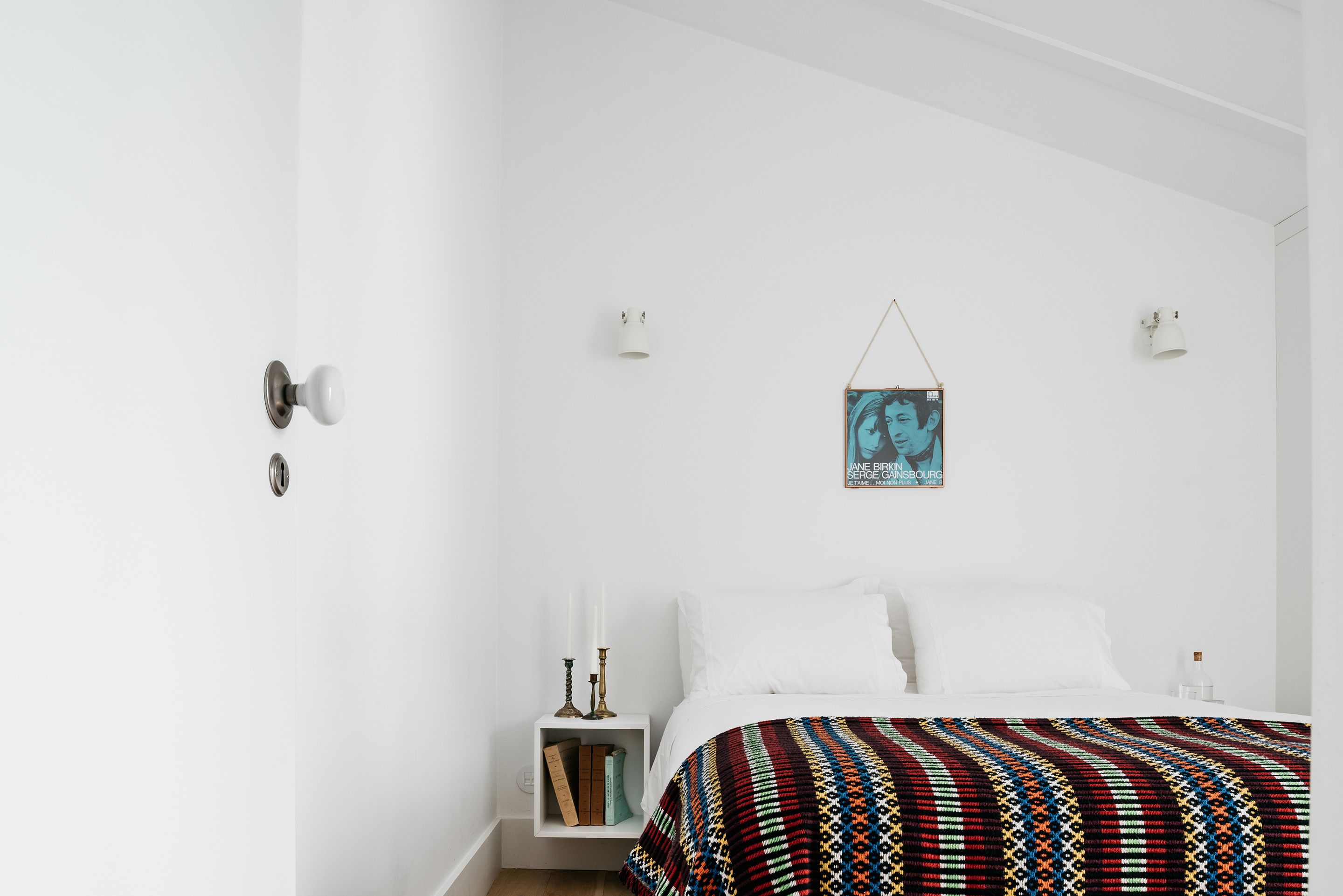 A minimalist bedroom with a bed, bedside tables, a wall-mounted picture, and a patterned bedspread.