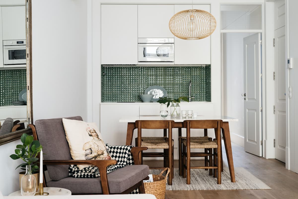 Une cuisine moderne avec des meubles blancs, un pare-feu vert et un coin repas comprenant des chaises en bois et une table blanche.