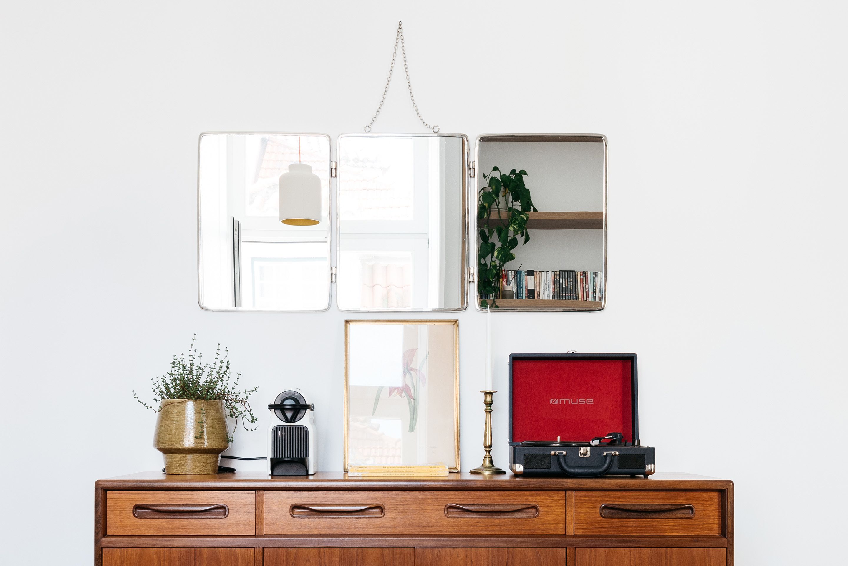 A wooden dresser with a potted plant, a framed picture, a vintage camera, and a red velvet case.