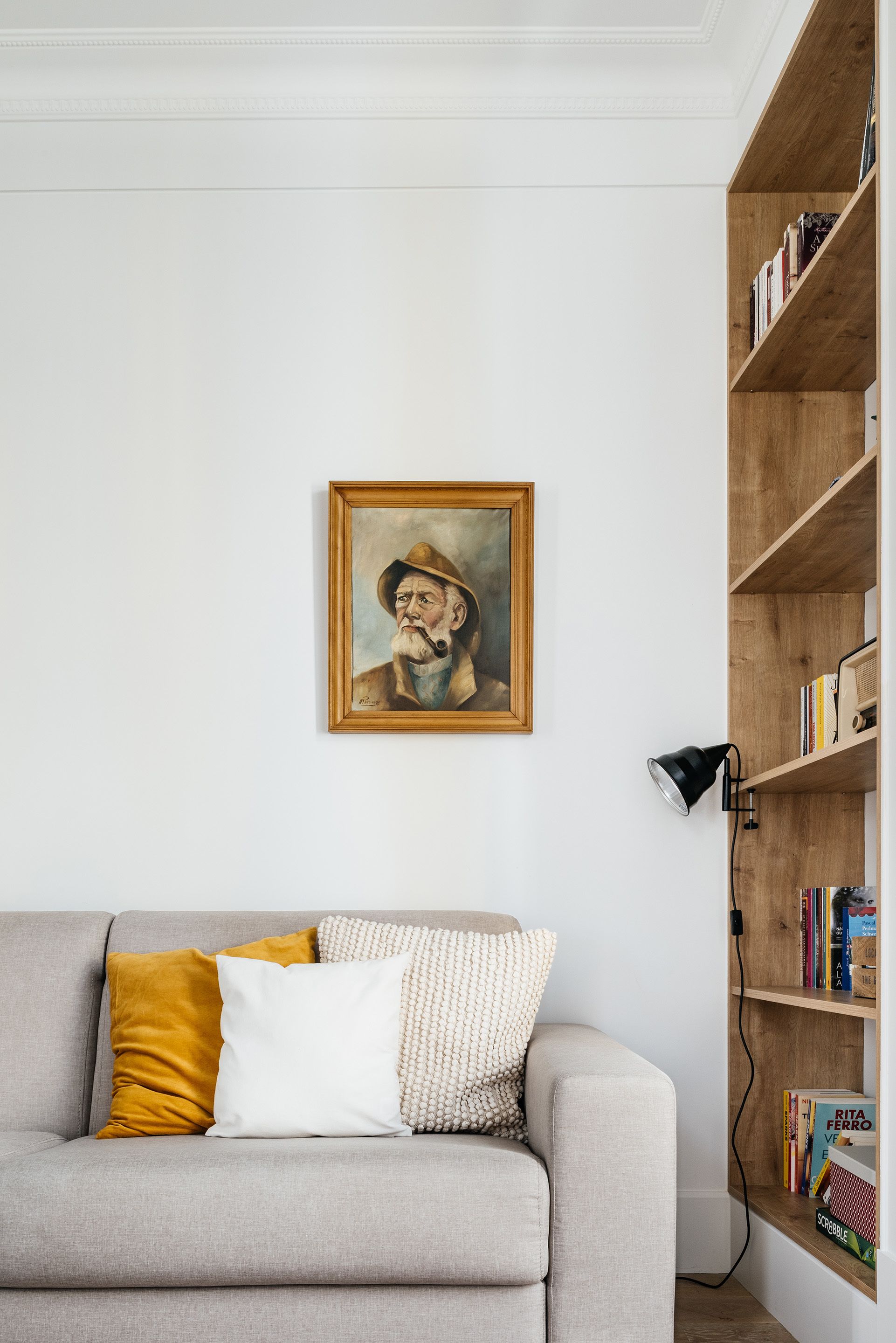 A living room with a grey sofa, a framed painting, a bookshelf, and a lamp.