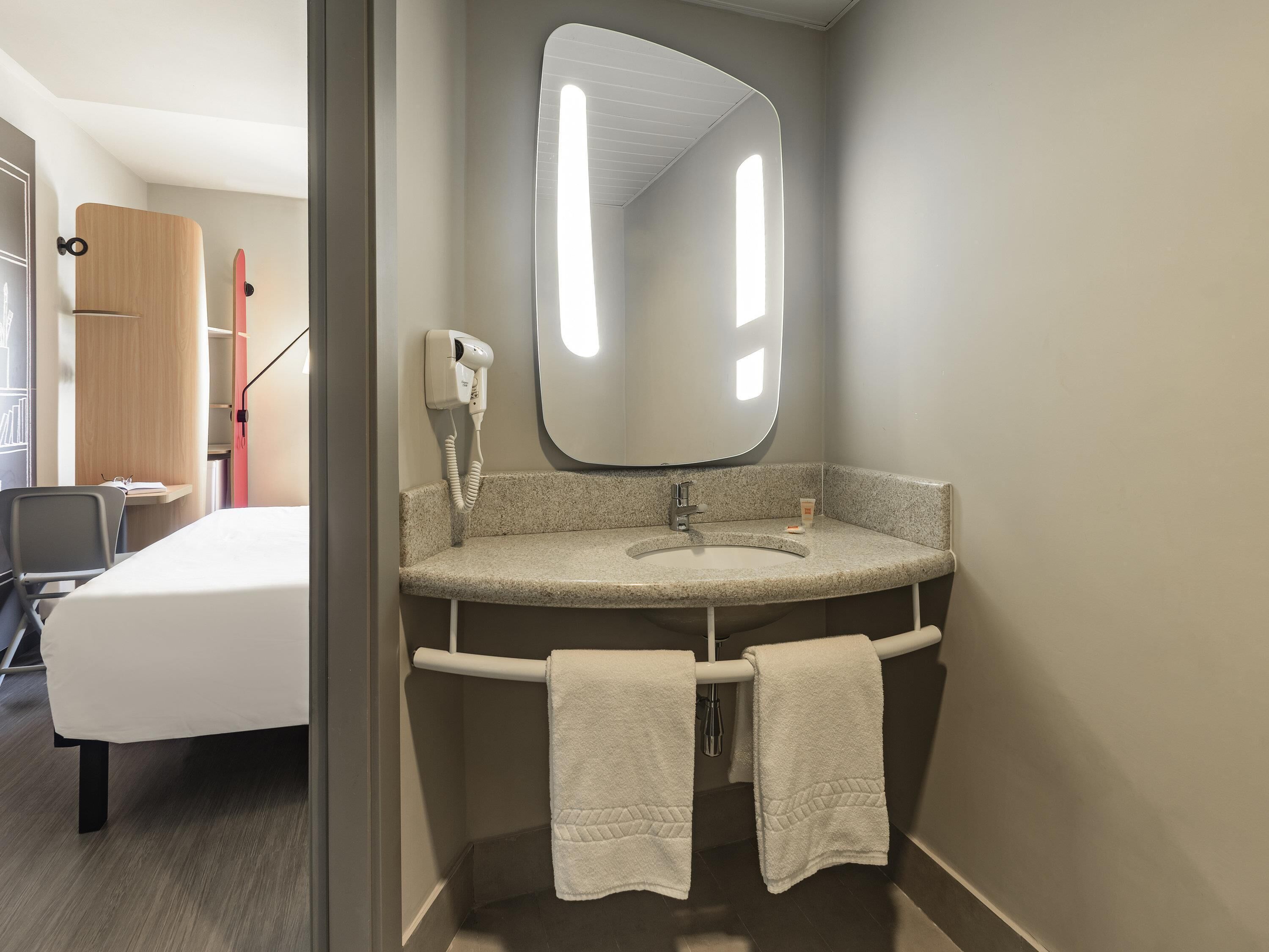A modern bathroom with a granite countertop, a large mirror, and two towels hanging on a towel bar.