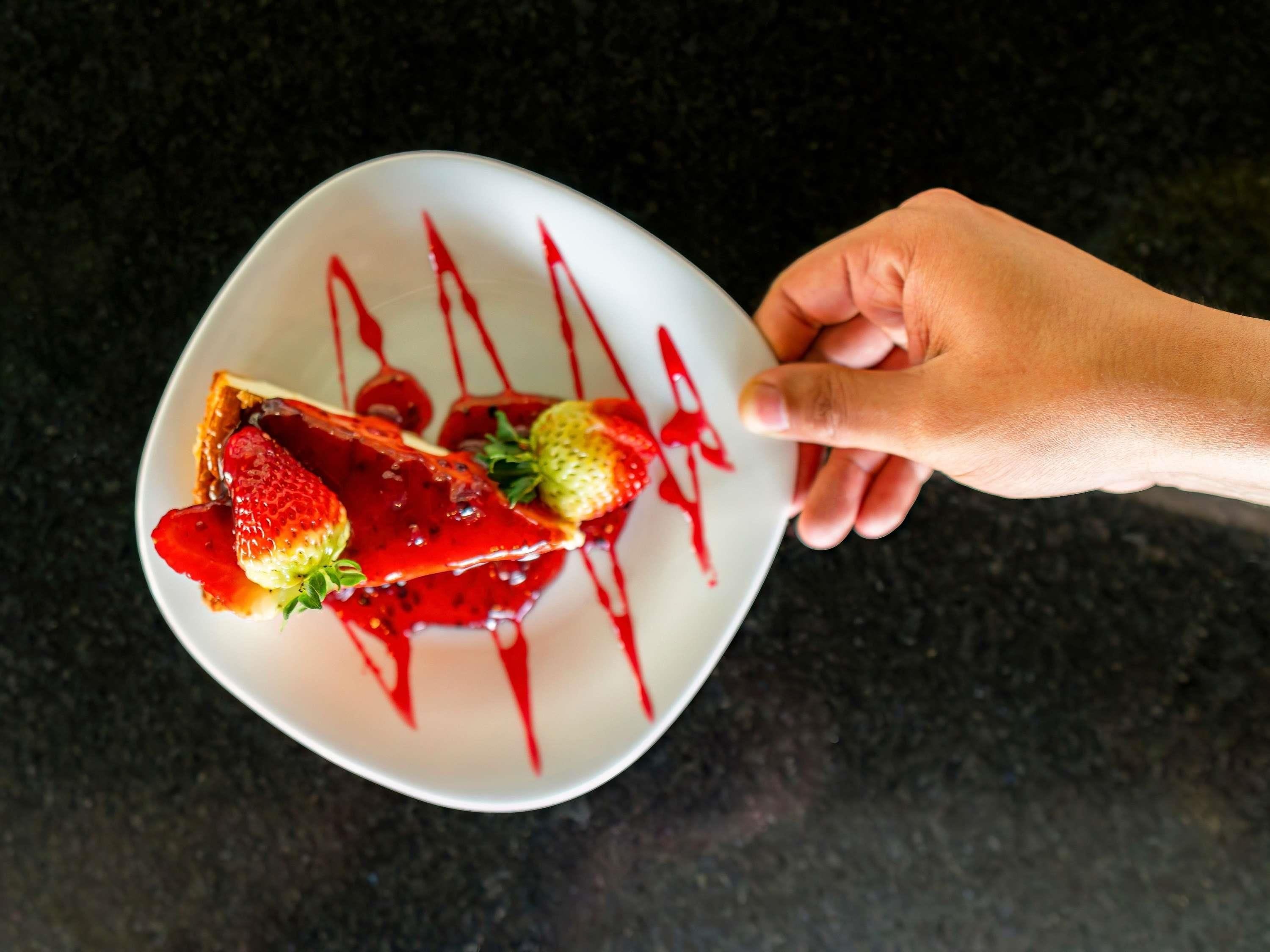 A hand holding a white plate with a slice of toast topped with strawberries and red sauce.
