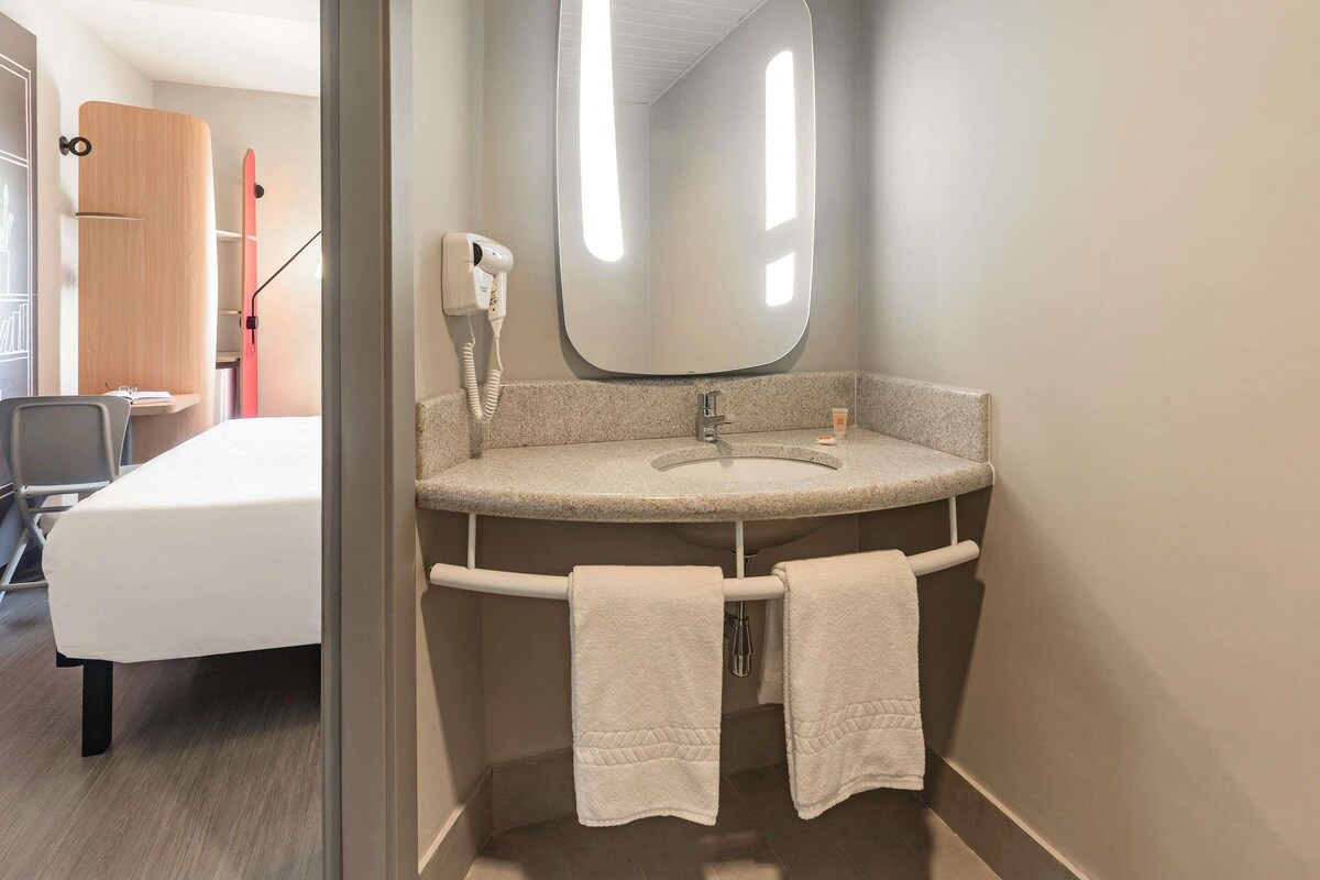 Un baño con un lavabo redondo, un espejo y dos toallas colgadas en un perchero.