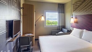 Habitación de hotel con una cama grande, un escritorio con silla, televisor, ventana con vistas y una lámpara.