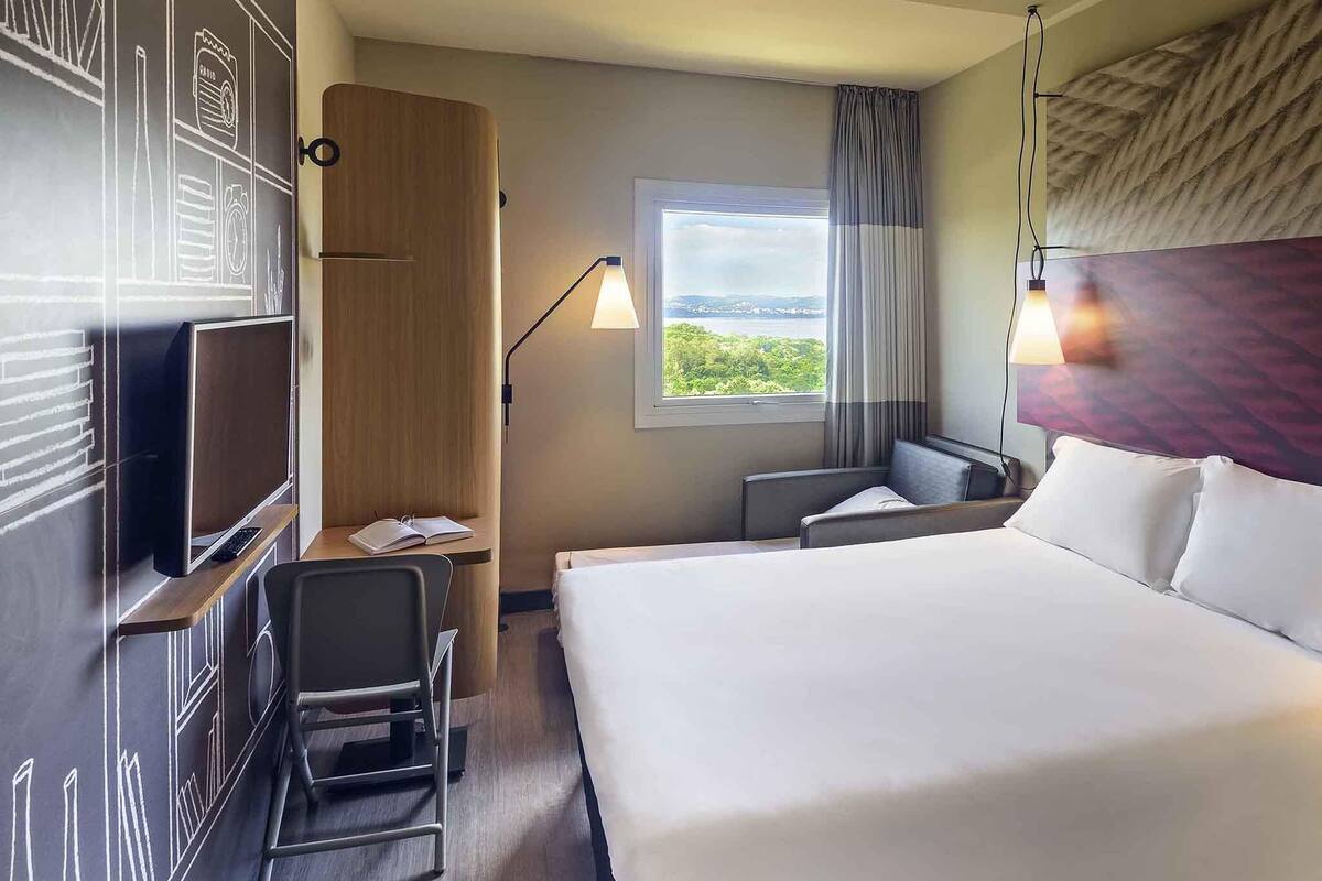 Hotelkamer met een groot bed, een bureau met stoel, een televisie, een raam met uitzicht en een lamp.