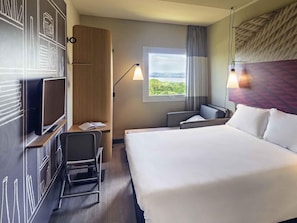 Une chambre d’hôtel avec un grand lit, un bureau avec une chaise, une télévision, une fenêtre donnant sur un beau paysage et une lampe.