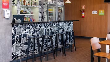 A bar area with a black and white mural, stools, and a refrigerator stocked with beverages.