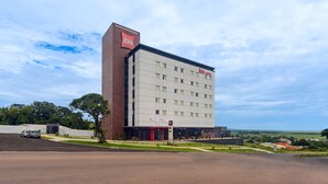 Un hotel moderno con un letrero llamativo de 'ibis', un amplio estacionamiento y vistas del paisaje circundante.