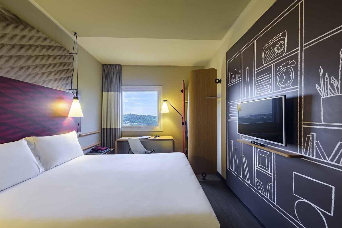 Een hotelkamer met een bed, een bureau, een televisie en een groot raam met uitzicht.