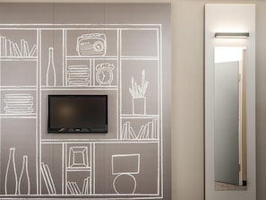 Pared con un televisor de pantalla plana montado sobre un mural tipo pizarra que muestra diversos objetos como libros, una radio y un reloj.