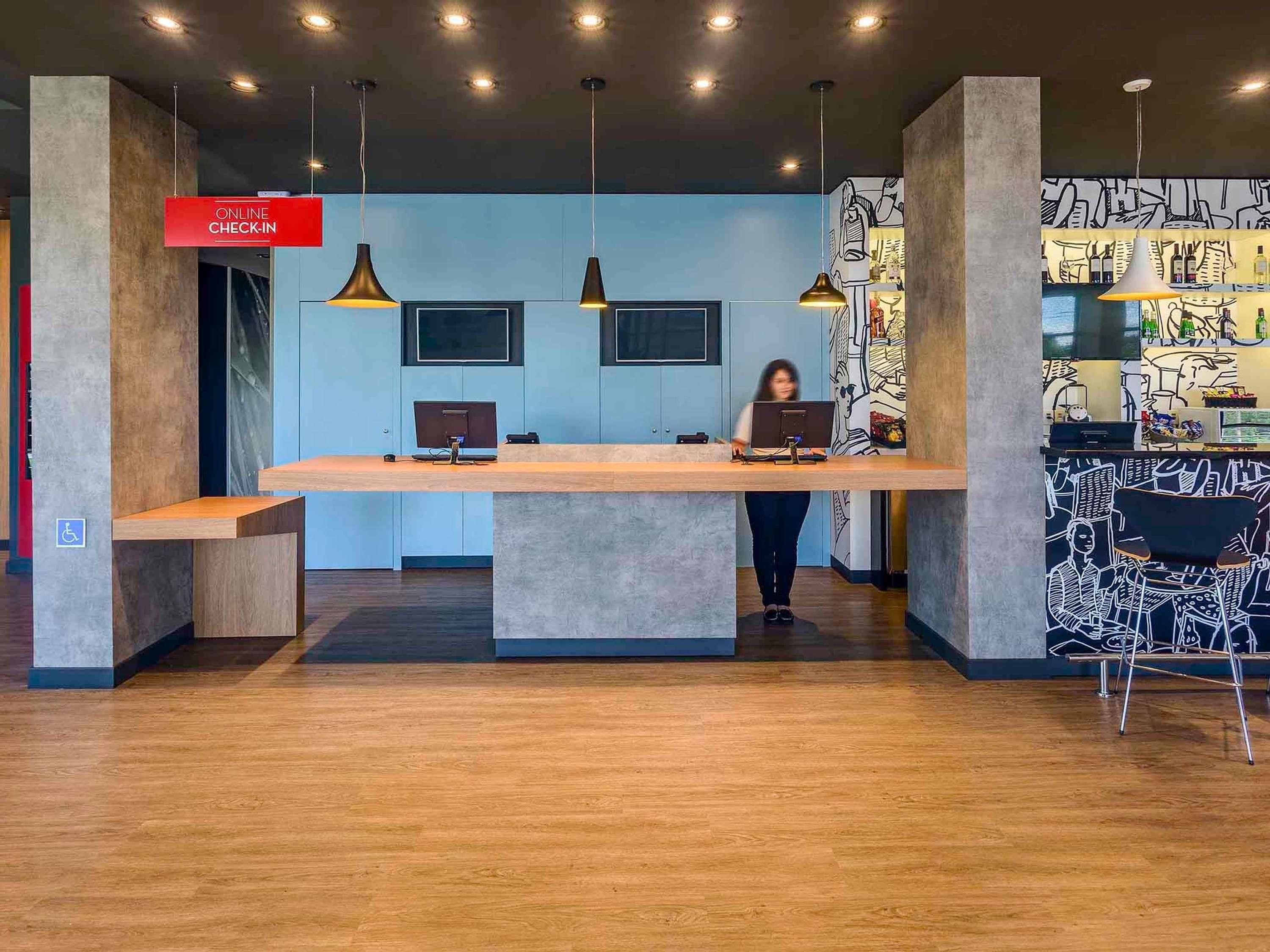 Un mostrador de recepción con dos computadoras, un cartel que dice 'ONLINE CHECK-IN' y un mural en la pared.