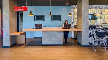 Un mostrador de recepción con dos computadoras, un cartel que dice 'ONLINE CHECK-IN' y un mural en la pared.