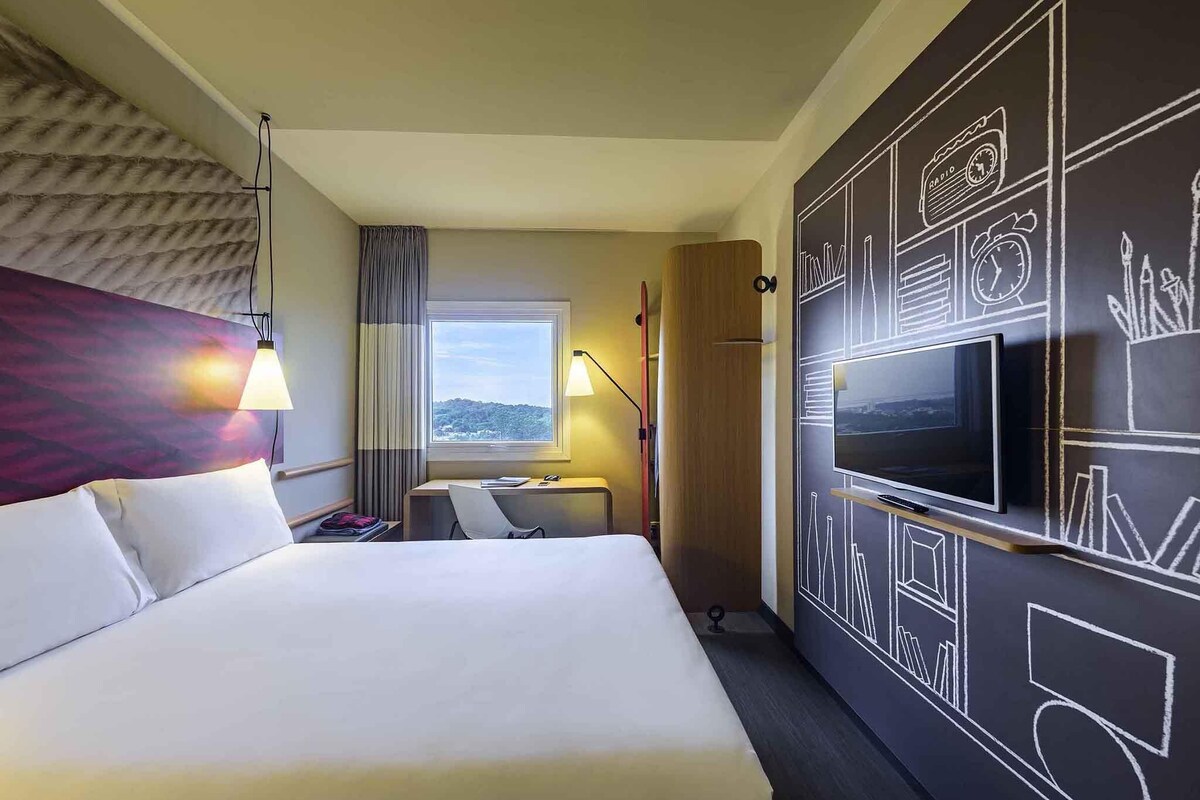 Habitación de hotel con una cama grande, un escritorio, un televisor y vistas al exterior.