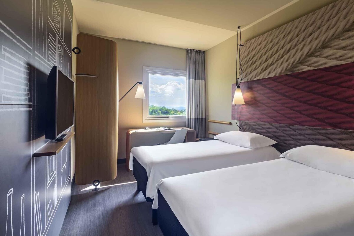 Habitación de hotel con dos camas, televisión, escritorio y ventana con vistas.