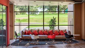 A modern interior with a curved sofa, red and white chairs, and a view of a green landscape through large windows. - ibis Guaiba (Guaiba)