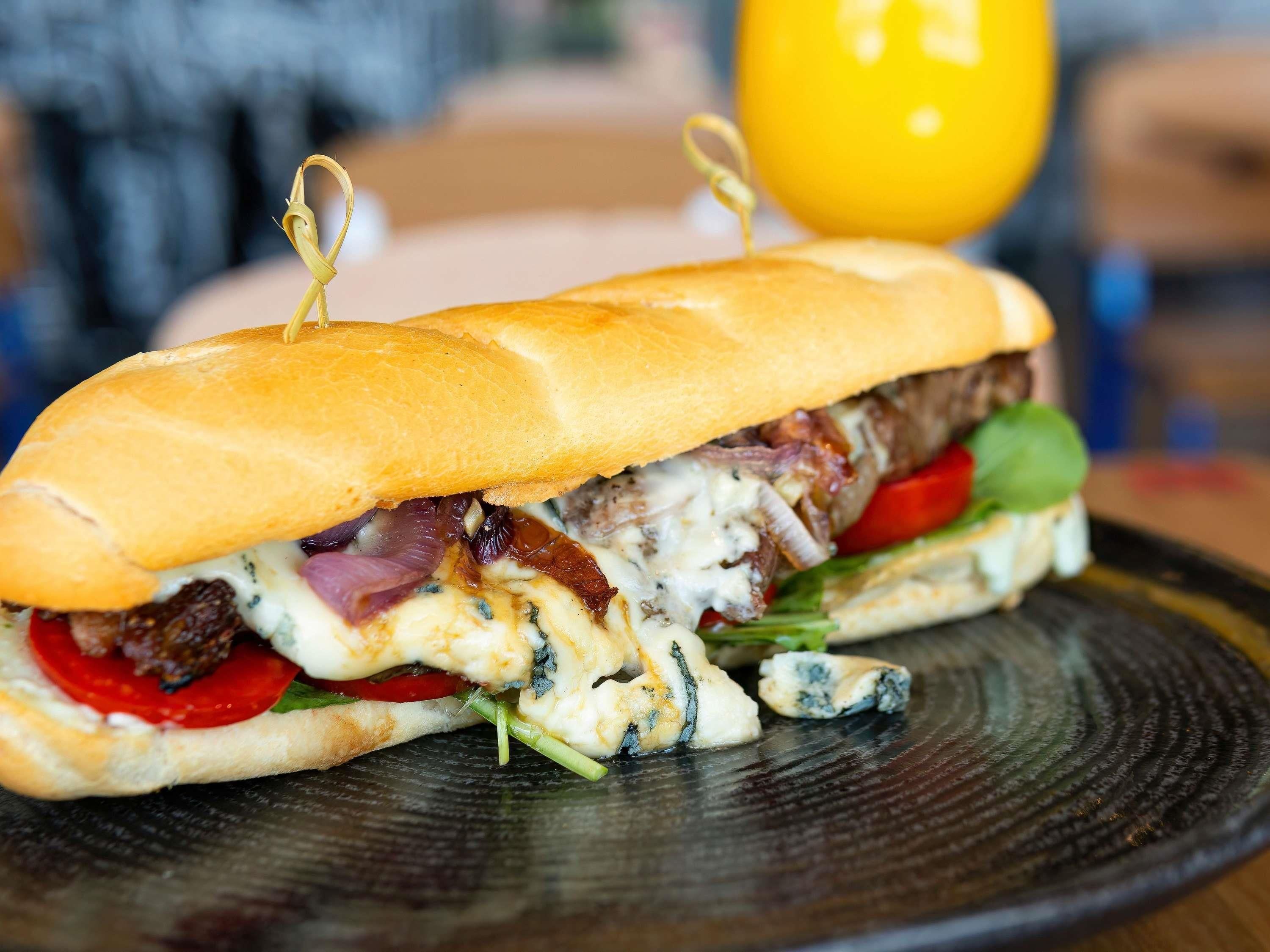 Un sándwich con un palillo encima, sobre un plato oscuro.