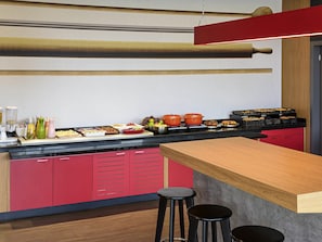Una cocina moderna con una encimera larga, armarios rojos y una barra con taburetes.