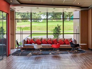 Un intérieur moderne avec un canapé aux lignes courbes, des fauteuils rouges et blancs, et une vue sur un paysage verdoyant grâce à de grandes fenêtres.
