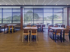Un comedor moderno con mesas y sillas de madera, ventanas amplias con persianas e iluminación empotrada en el techo.