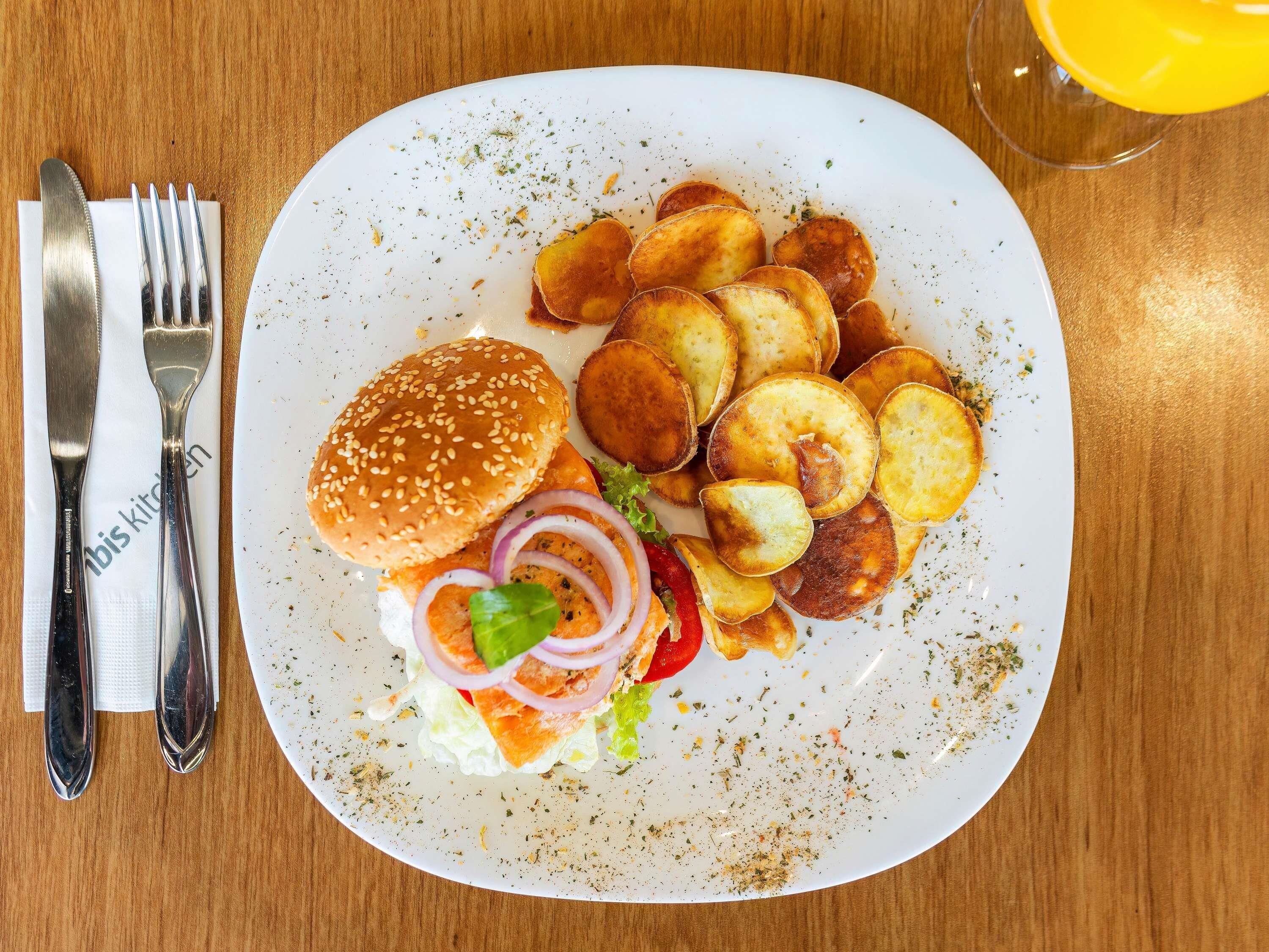 Un plato con una hamburguesa, papas fritas y un vaso de jugo de naranja sobre una mesa de madera.