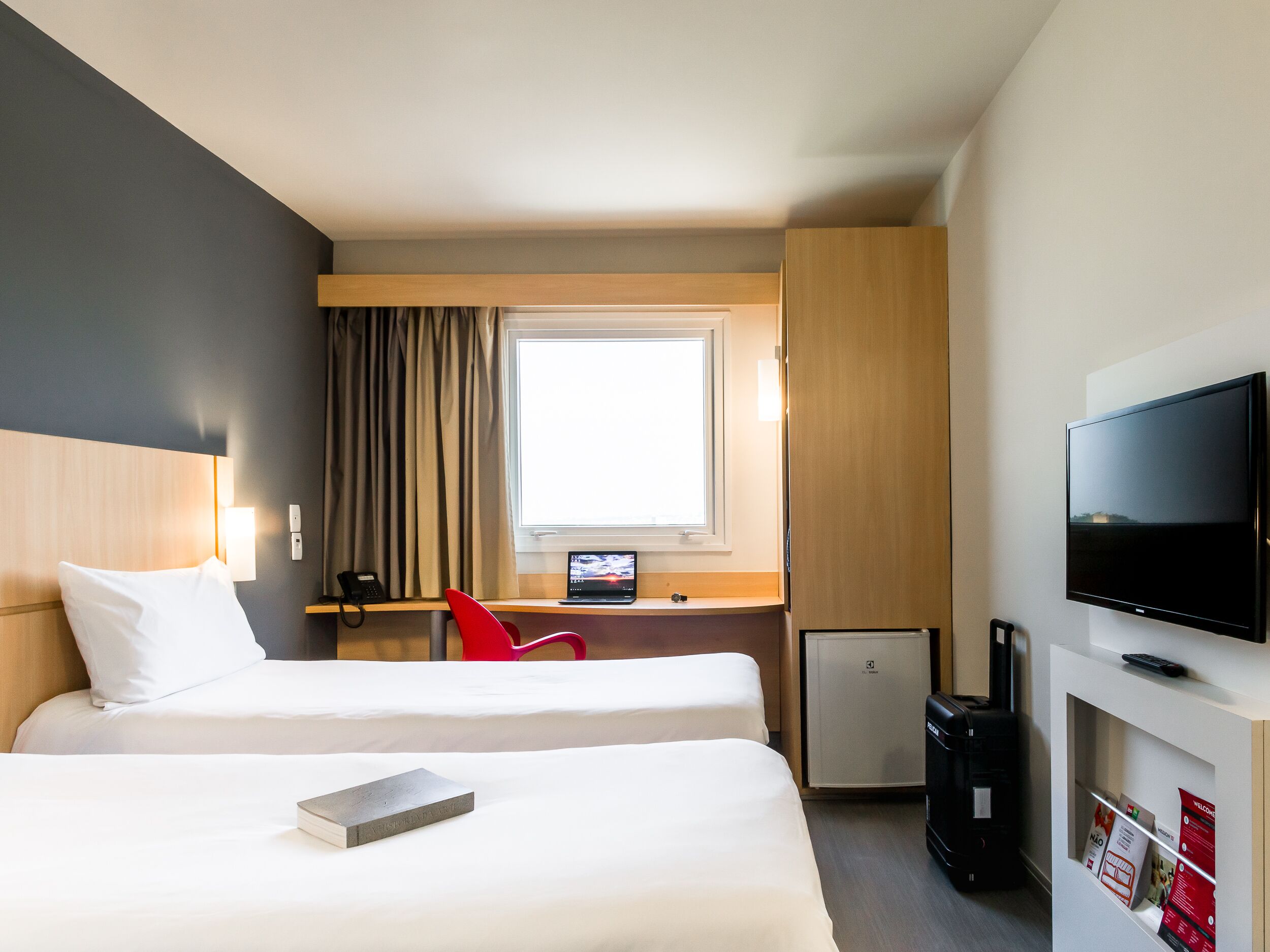 A hotel room with two beds, a desk with a computer, a TV, and a minibar.