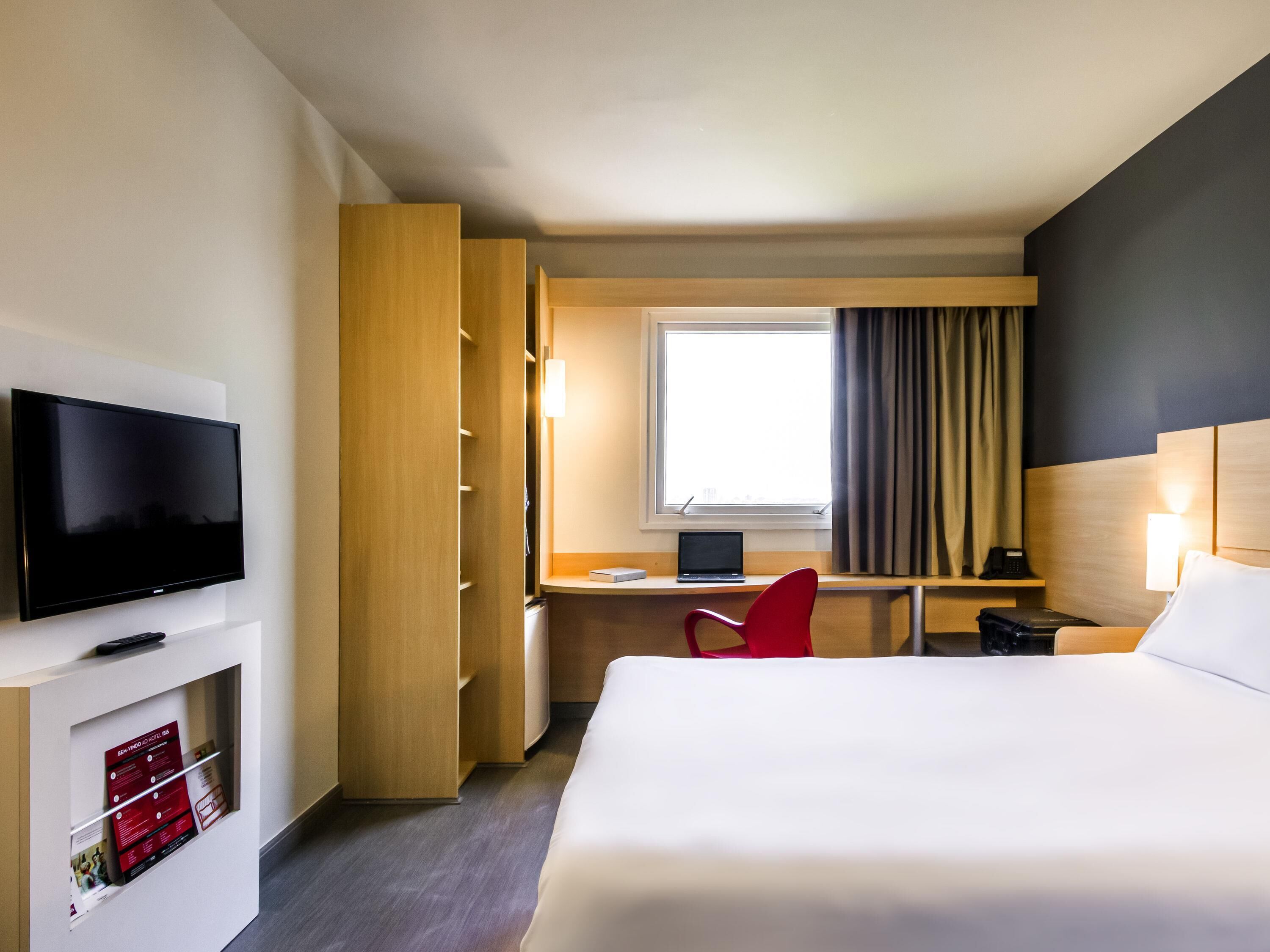 A hotel room with a bed, a desk, a TV, and a wardrobe.