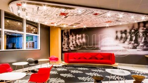 Un área de descanso moderna con un sofá rojo, sillas rojas y un mural con un tablero de ajedrez.