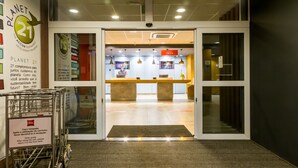 Zona de recepción de hotel con mostrador de registro, un carrito y un cartel que indica registro en línea.