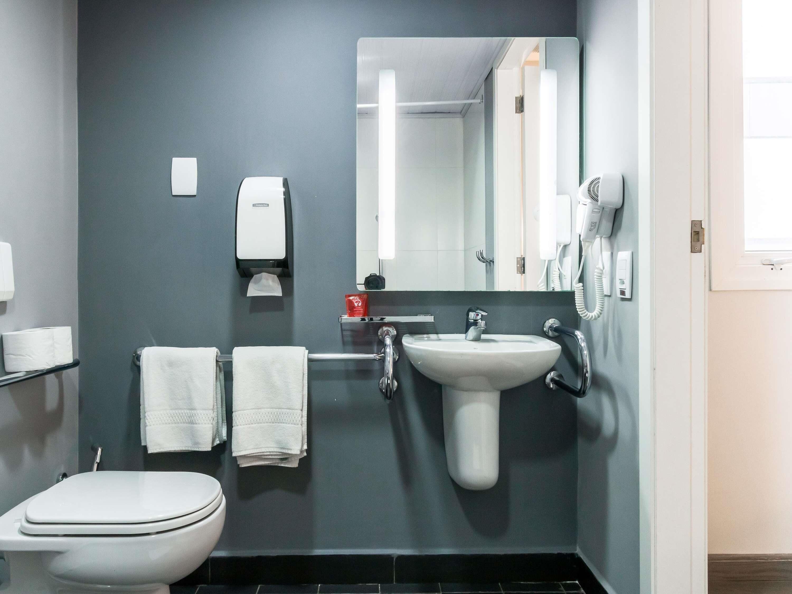 Un baño con inodoro, lavabo, toallero, secador de manos y espejo.