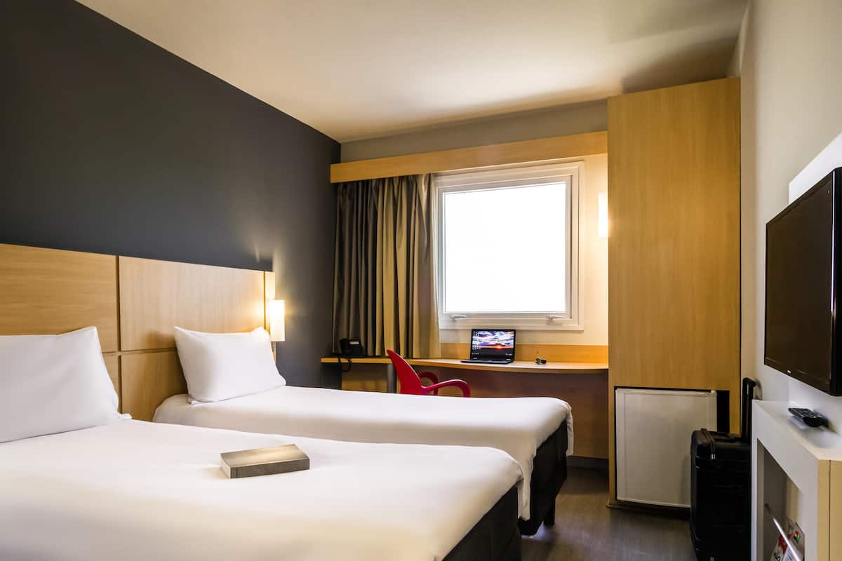 A hotel room with two beds, a desk with a laptop, a TV, and a small fridge.