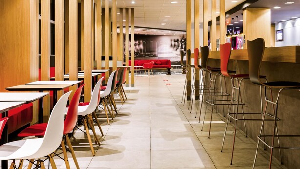 Un restaurante moderno con separadores de madera altos, sillas rojas y blancas, y una barra larga.