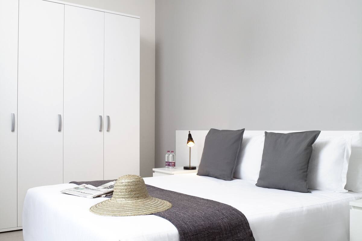 A modern bedroom with a large bed, white wardrobe, and a bedside lamp.