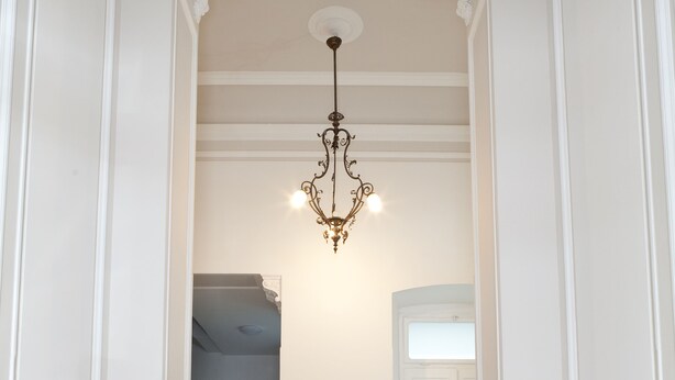 A hallway with a chandelier, a statue on each side, and a potted plant. - Palazzo Talenti 1907 (Trieste)