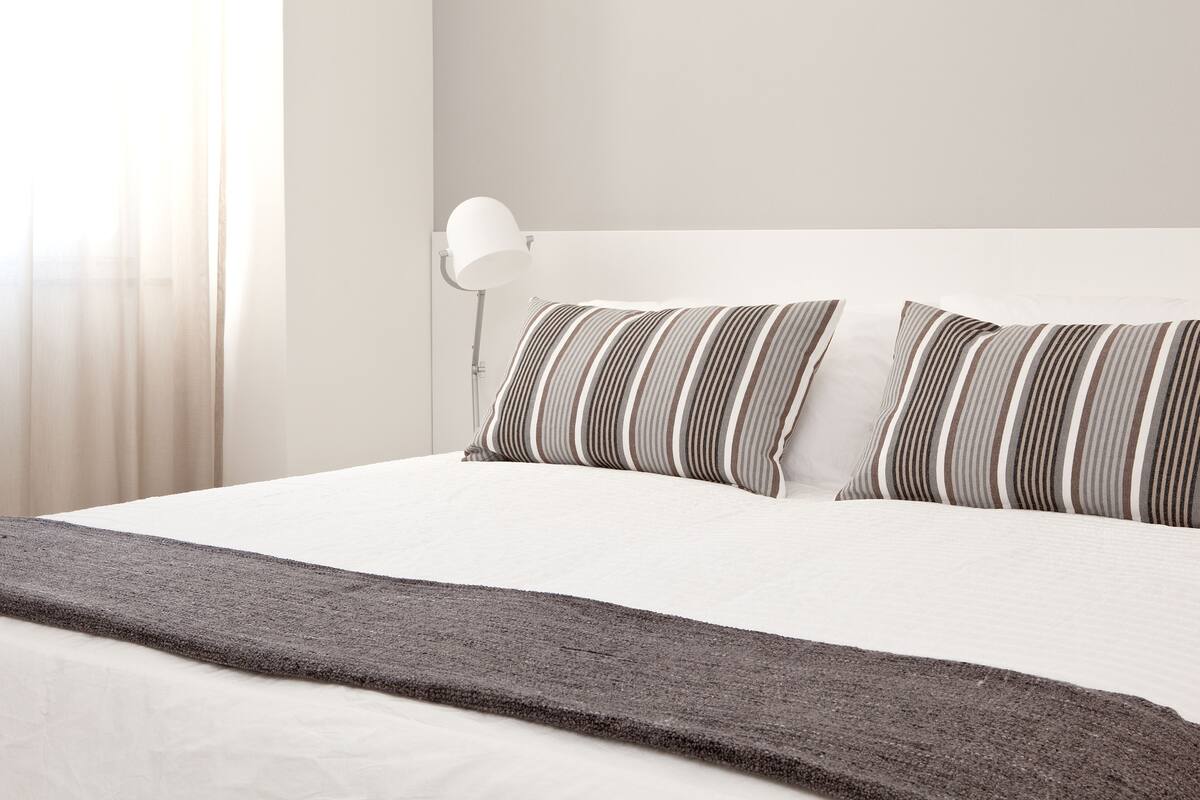 A neatly made bed with striped pillows and a gray throw blanket.