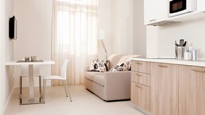 A modern, well-lit kitchen with a microwave, cabinets, and a dining area with a table and chair. - Palazzo Talenti 1907 (Trieste)