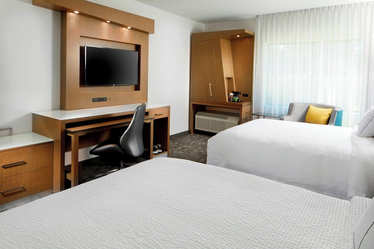 Een hotelkamer met twee bedden, een bureau met stoel, een televisie en een minibar.