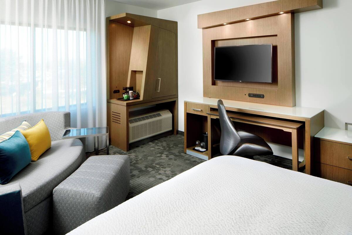 Een hotelkamer met een bed, een bureau, een stoel, een televisie, een kledingkast en een bank met kussens.