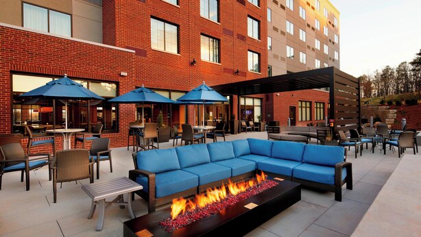 An outdoor patio area with a fire feature, seating arrangements, and a covered section with umbrellas. - Courtyard by Marriott Charlotte Fort Mill, SC (Fort Mill)