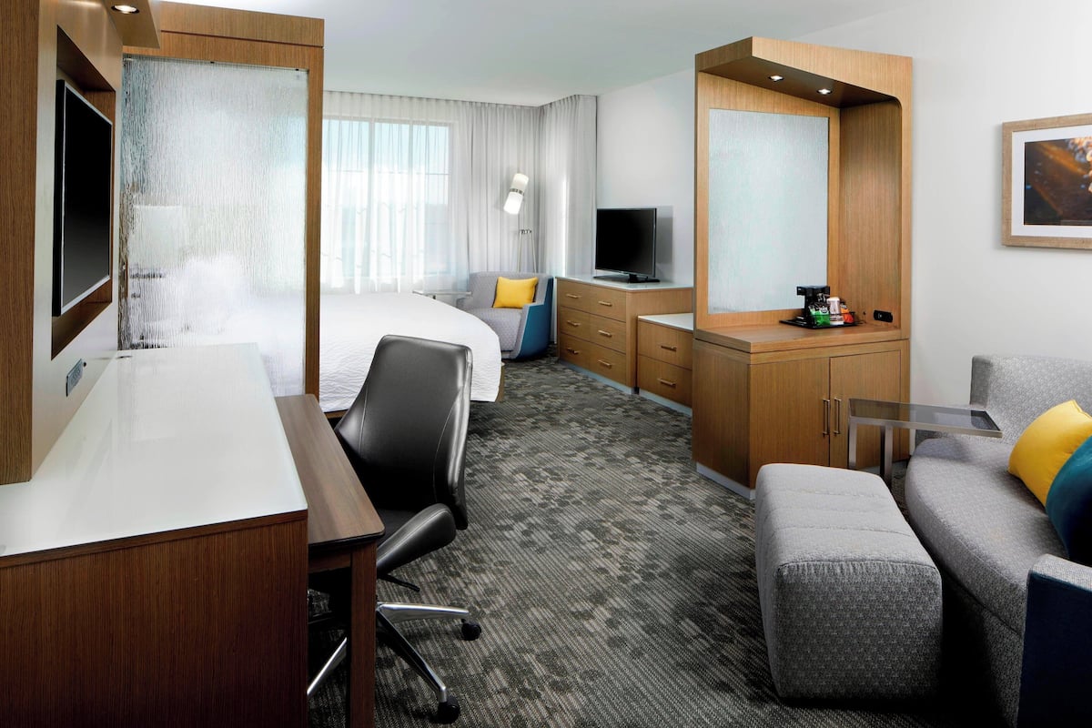 Een hotelkamer met een bed, een bureau, een televisie, een bank en een kleine tafel met een koffieapparaat.