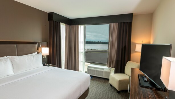 Une chambre d’hôtel avec un grand lit, un bureau avec une télévision, une chaise et une vue sur une étendue d’eau par la fenêtre.