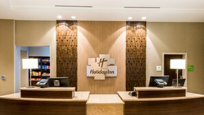 Un comptoir d’accueil d’un hôtel Holiday Inn, avec deux guichets, un décor mural en bois et une enseigne au-dessus des guichets.
