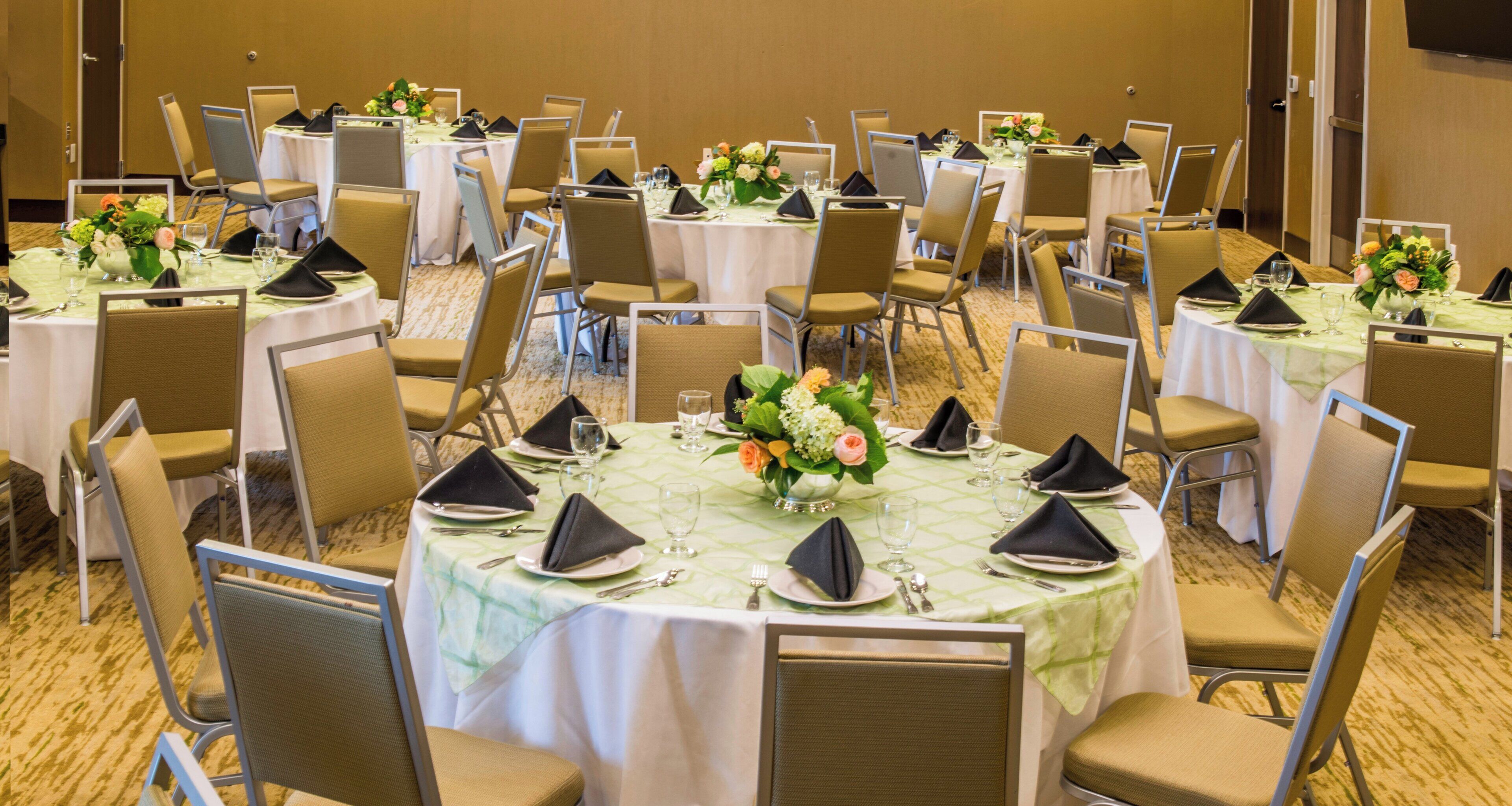A conference room with round tables, chairs, and floral centerpieces.