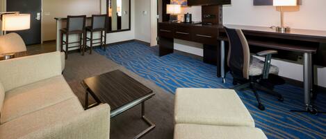 A hotel room with a seating area, a desk, a television, and a painting on the wall.