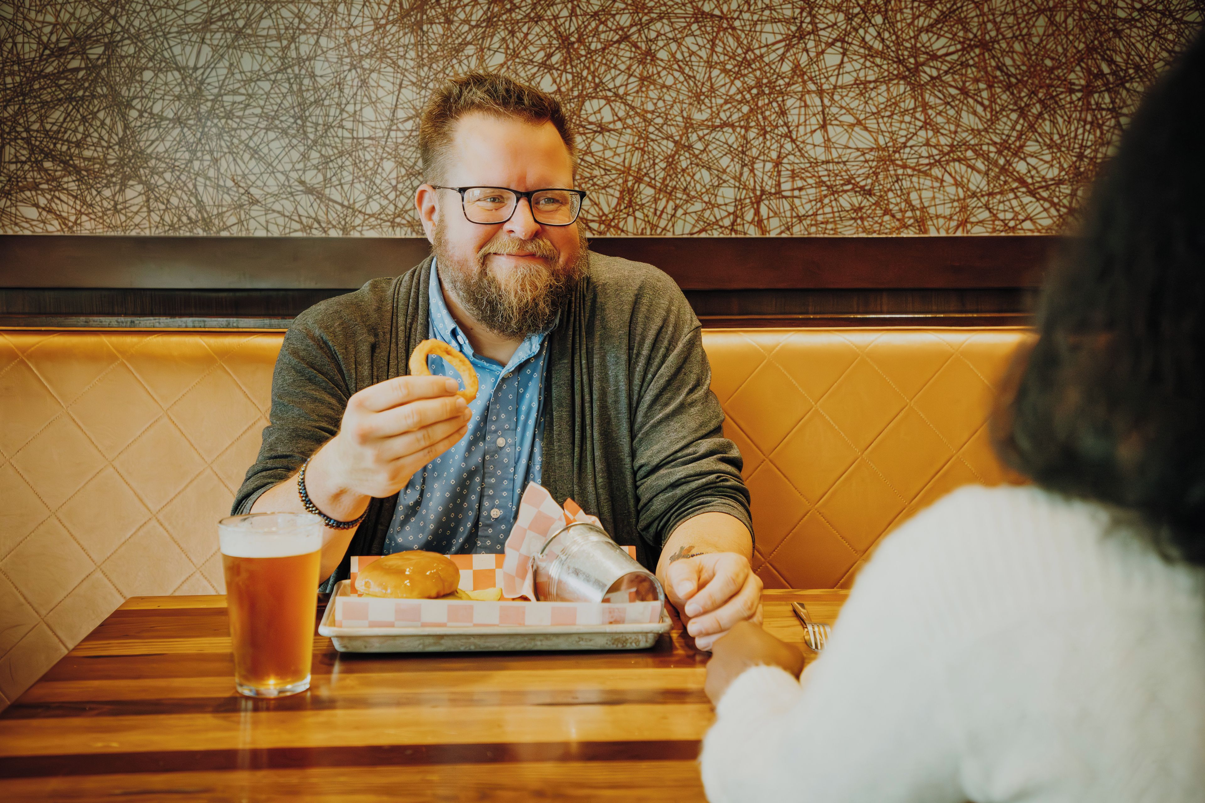 A person seated at a table with a plate of food, a glass of beer, and a menu.