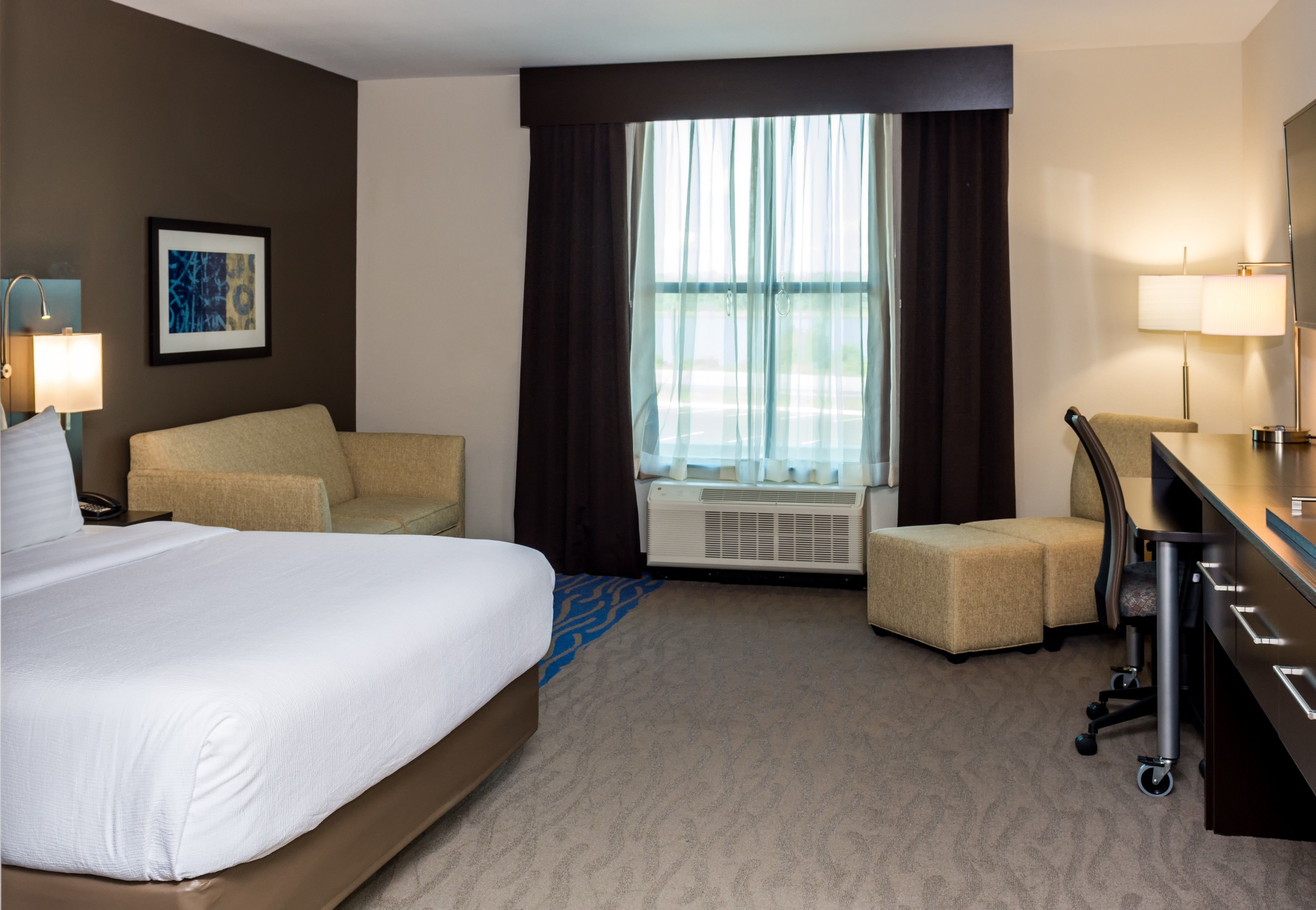 A hotel room with a bed, a desk, a chair, and a window with curtains.