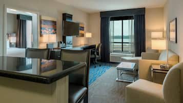 A hotel room with a dining area, a bed, a desk, a chair, a sofa, and a view of the outdoors.