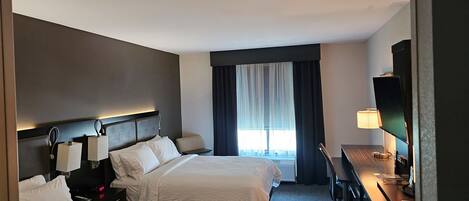 A hotel room with two beds, a desk, a television, and a window with curtains.